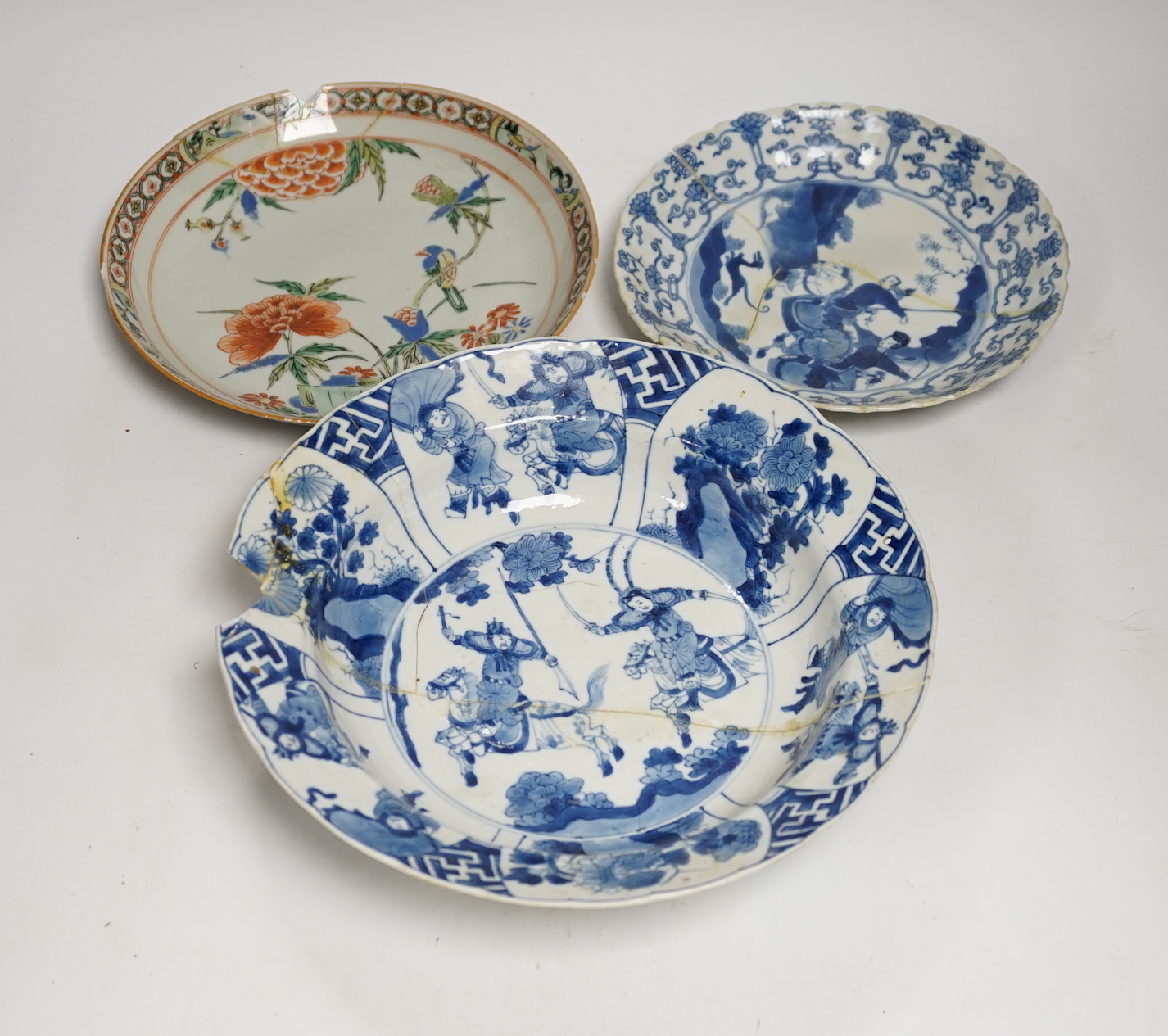 A Chinese blue and white ‘warriors’ bowl, Kangxi mark and period, a similar ‘hunting’ saucer dish, and a famille verte saucer dish, all Kangxi period (3), largest 27cm in diameter